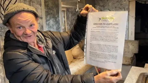 ANDREW TURNER/BBC John Smith hold up his eviction paper served by Norfolk County Council.