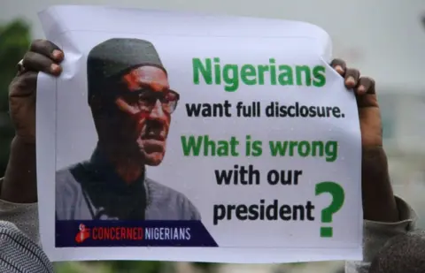 AFP/Getty Images A Nigerian protester pictured on 7 August 2017 shows a placard reading, "Nigerians want full disclosure. What is wrong with our president?"
