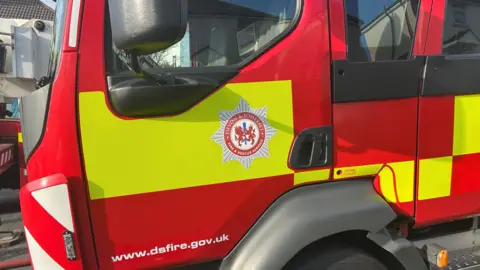 Close up shot of a Devon and Somerset Fire Service engine at the scene of an incident. The vehicle is red and yellow and has the service's emblem on the door.