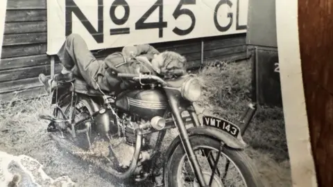 Handout Gordon Talbot is seen in a black and white photograph from the 1940s lying on his back on a motorbike.
