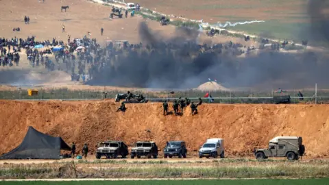 AFP A picture taken from the southern Israeli kibbutz of Nahal Oz shows Palestinian men protesting on the other side of the border with Gaza (6 April 2018)