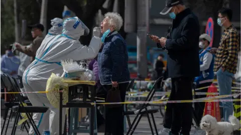 Getty Images A health worker wears protective gear as she gives a nucleic acid test to detect COVID-19 on a local resident at a mass testing site after new cases were found, on April 6, 2022 in Beijing, China.