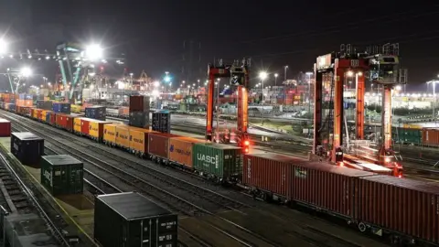 Rail tracks with containers on freight trains at night with dozens of flood lights