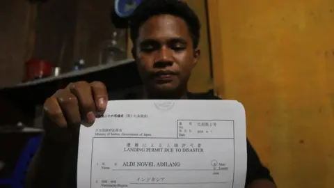 AFP Mr Adilang holds a document showing he was allowed to land in Japan "due to disaster"