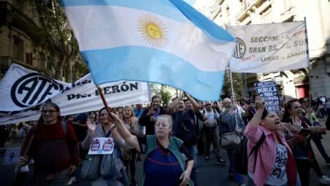 Reuters A middle-aged woman waves a large Argentinian flag during a protest against university cuts in Buenos Aires.