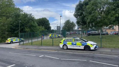 A street scene showing three police cars outside of a school gate.