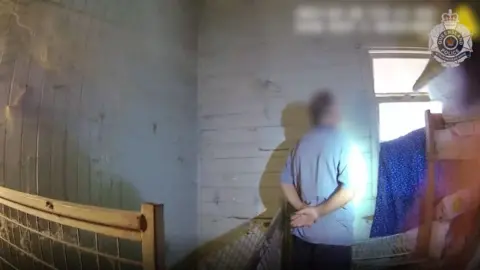 Queensland Police Man in blue shirt and shorts standing in a derelict room