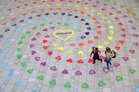 Ben Birchall/PA Media A mother and daughter walk over a spiral pattern of rainbow-coloured hearts