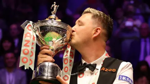 Getty Images Kyren Wilson celebrates winning the World Championship by kissing the trophy