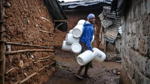 Getty Images A woman is seen carrying her water Jerrycans past the corridors in Kibera Slums.