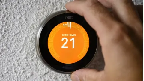 Getty Images A photo illustration of a hand adjusting a Google Nest smart thermostat to adjust the temperature in the living room on October 12,2021 in Kampen, Overijssel, The Netherlands .