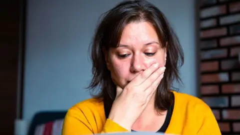 Getty Images Anxious woman looks at bills