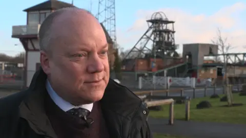 Mr Prior smartly dressed in a tie and shirt in front of an old mining facility 