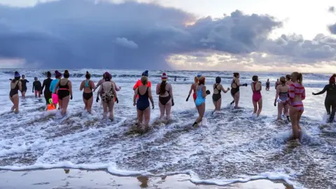 PA Media Picture showing a number of women in swimming costumes standing in shallow water at King Edward's Bay near Tynemouth on the north east coast