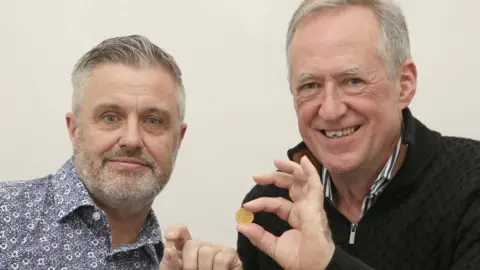 Dix Noonan Webb Metal detectorists Mark Pallett and Andy Carter, both holding up a gold coin each