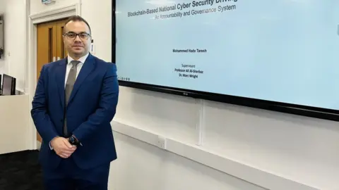 University of Gloucestershire Mohamed Hady standing in front of a cyber security presentation
