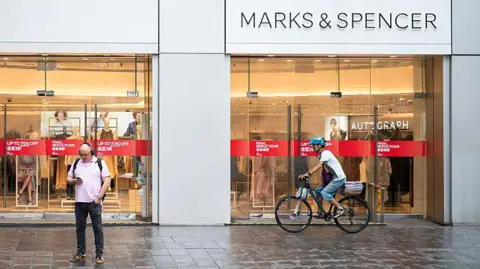 Pedestrian on phone and a cyclist outside Marks and Spencer shopfront