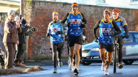 Getty Images Kevin Sinfield runs through a street flanked by a support crew and cheered on by members of the public.