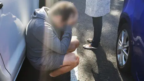 AFP A suspect in custody kneels down and holds his head