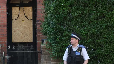 Arrest over suspected arson on properties linked to PM 10 Reuters A police officer stands outside a house with a boarded-up door