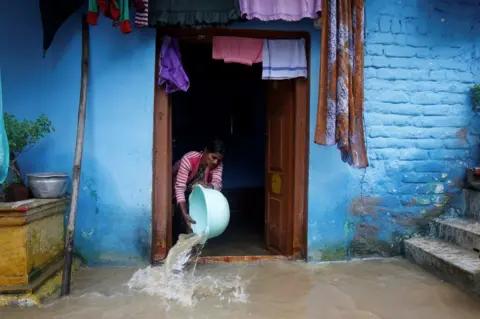 AFP A woman tries to clear floodwaters from her home in Hunsur town in the southern state of Karnataka on 10 August 10 2019