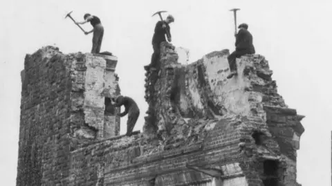 Men in black and white image pick-axing an old jail in the 19th C