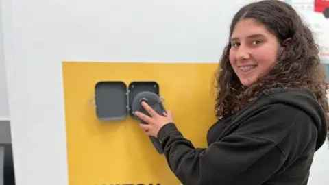 S1 pupil Clara wearing a black jumper unlocks her phone from a Yondr pouch after they were introduced at Portobello High School.