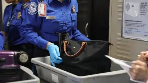 Getty Images An anonymous TSA official checks a bag in a luggage tray