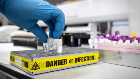 Getty Images gloved hand in testing lab with sign reading danger of infection