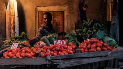 AFP A woman makes a selection of the most expensive tomatoes for a customer just before the 7PM curfew in Kibera, Nairobi on May 05, 2020.