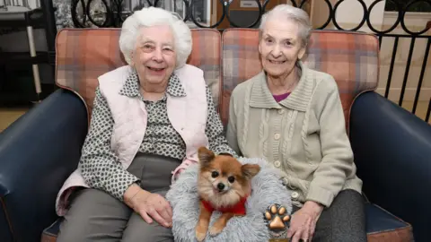 Colne View Two women sitting on a sofa with a small Chihuahua 