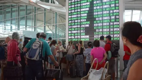 EPA Passengers watch the information board at Bali"s International Airport