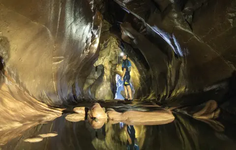 Jane Barlow / PA Media Cameron Smith explores Stalactite Cave, which forms part of a network of caves under the Arbroath Cliffs on the Angus coast of Scotland, on 20 July 2021