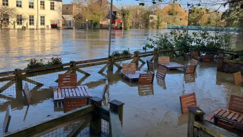 Tables and chairs outside a restaurant submerged in flood water.