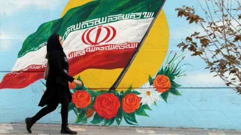 Getty Images A woman walking in front of a mural featuring the Iran flag