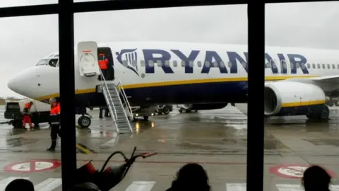 Reuters Travellers wait in front of a passenger jet belonging to Ryanair