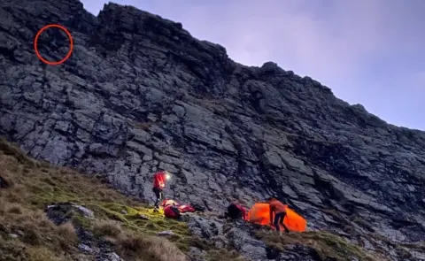 Keswick Mountain Rescue Team Picture shows the rescue team on the ground with the man, with a red circle marking where the woman was stuck