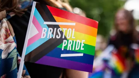 B A pride flag reading 'Bristol Pride' sticks out from an attendee's bag