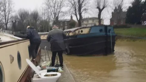 John Aston Two volunteers on the vessel after it has been secured. Another barge can be seen passing along the river. 