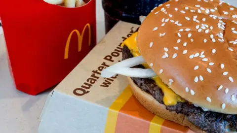 Getty Images A quarter pounder with cheese, fries, and a drink arranged at a McDonald's restaurant in El Sobrante, California, USA, on Oct. 23, 2024.  The McDonald's quarter pounder sits on a takeaway box with a bit of cheese and onion peeking out from under the bun. A red box for fries sits to the left.