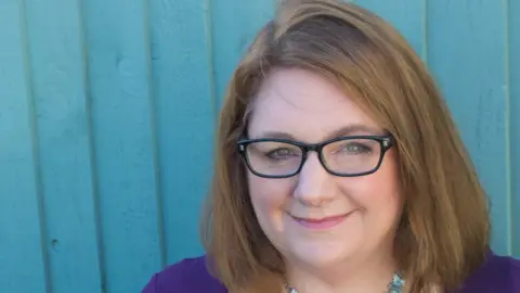 Bekka Prideaux Bekka Prideaux headshot taken against a wooden fence, which is painted turquoise. She has brown/blonde hair in a bob and wears funky black glasses, and a blue blouse. She is smiling at the camera.