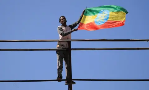 Reuters A man standing in an elevated position flies the Ethiopian national flag.