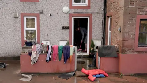 PA Media A man cleaning up after his house was flooded