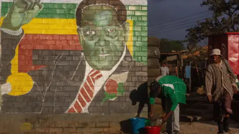 Getty Images People in Mbare, Harare, by a mural of Zimbabwe's late President Robert Mugabe - 2019