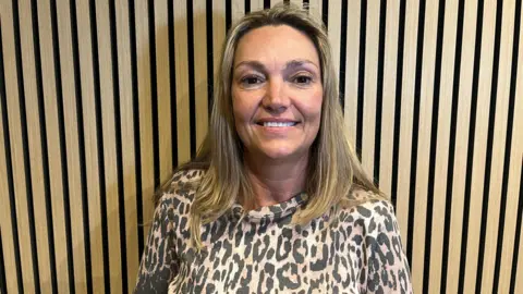 Mandy is wearing a leopard print top. She has shoulder length light-brown hair. 