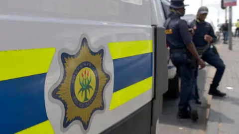 A South African police-branded vehicle is seen next to officers