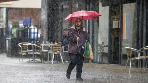 PA Media A woman shelters under an umbrella during a heavy downpour of rain in Belfast. Picture date: Monday July 31, 2023.