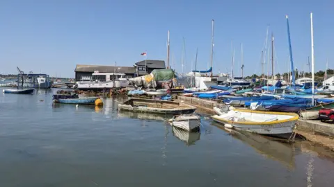 Peter Walker/BBC Small boats and yachts moored up on the water at West Mersea with bright blue skies above.