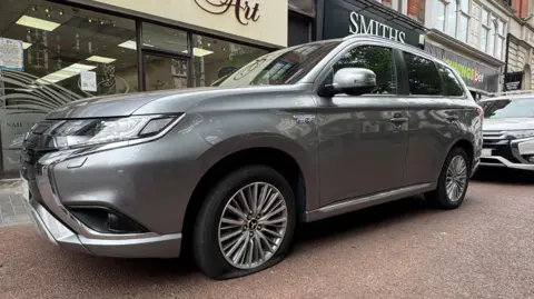 A silver Mitsubishi SUV with a flat tyre.