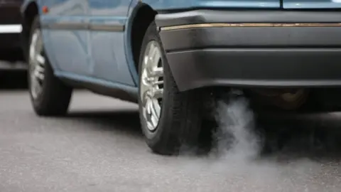 AFP The exhaust pipe of a blue car with white smoking coming out.